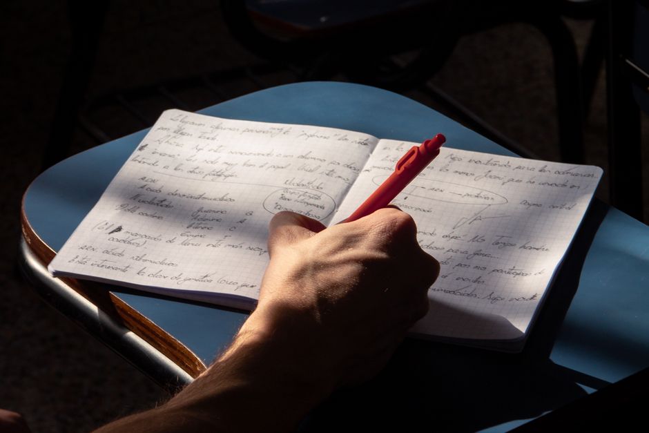 Manos escribiendo notas junto a una computadora portátil encendida
